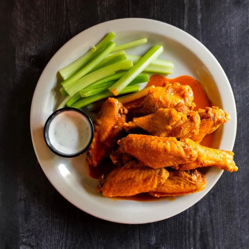 Plate of buffalo chicken wings with celery and dipping sauce.