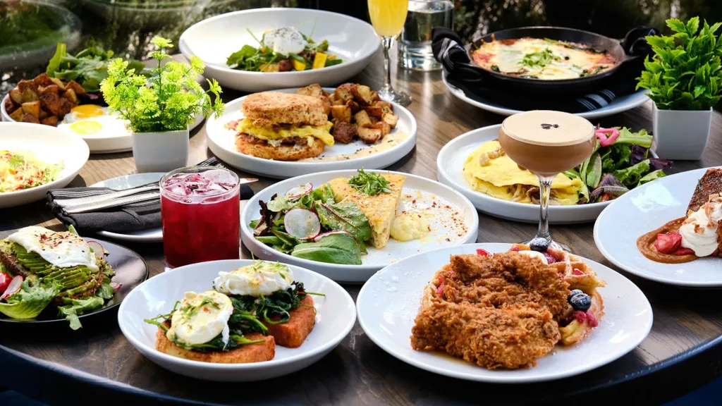 A table laden with various brunch dishes, drinks, and green plants.