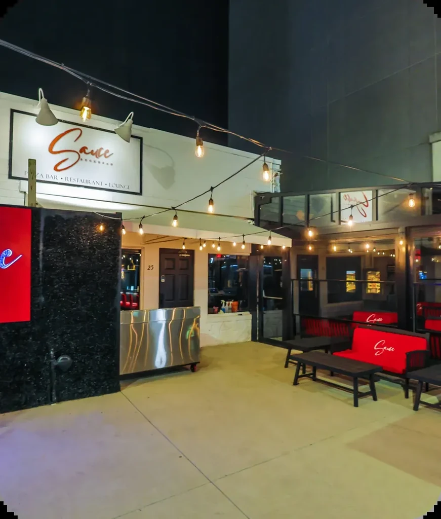 Sauce Pizza Bar exterior at night with illuminated patio and sign.