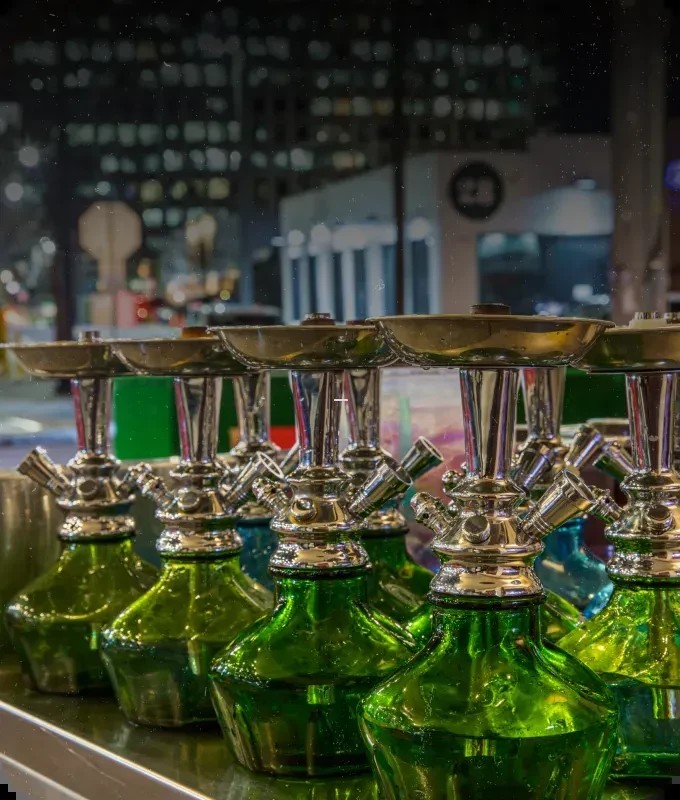Row of green and blue hookahs on a reflective bar at night.