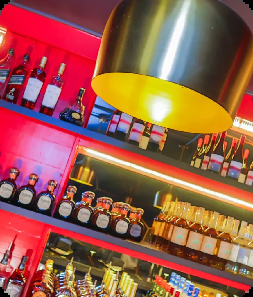 Numerous alcohol bottles on red lit shelves with a glowing gold pendant light.