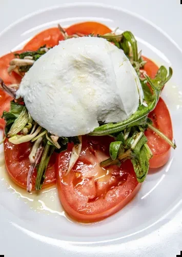 Fresh burrata cheese, sliced red tomatoes, and greens with olive oil.