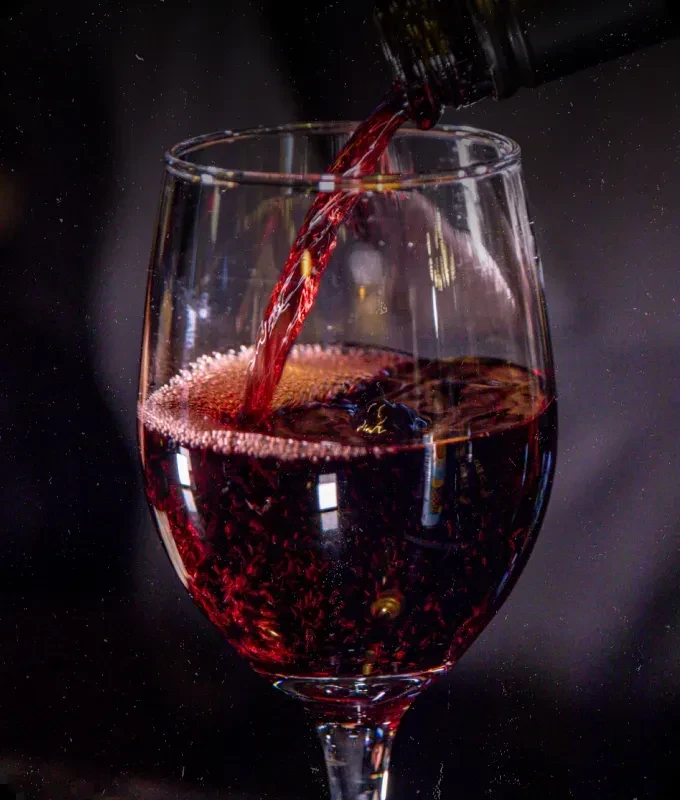 Deep red wine pours into a glass, creating froth.