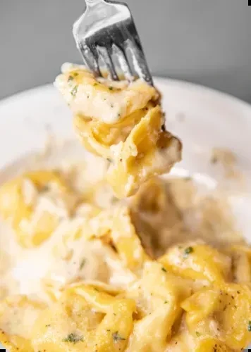 Fork lifting golden pasta with creamy sauce and green herbs.