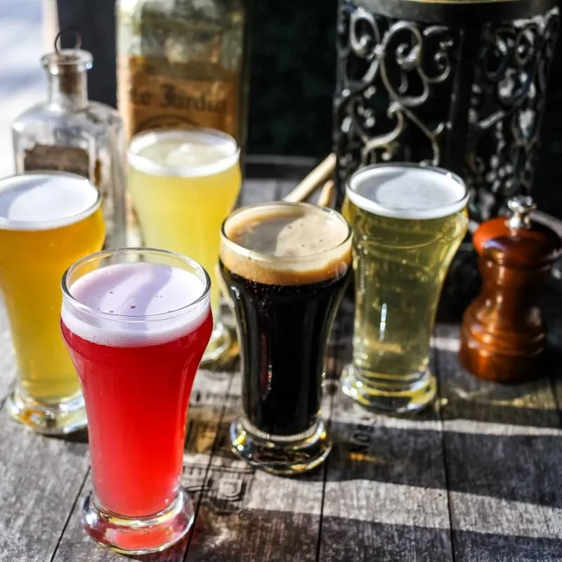 Five varied drinks in tasting glasses on a rustic wooden surface.