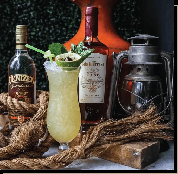 Rum cocktail flanked by two rum bottles with coiled ropes.