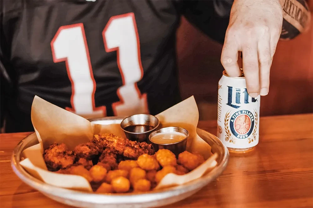 Crispy chicken, tater tots, and a hand opening a pilsner beer.