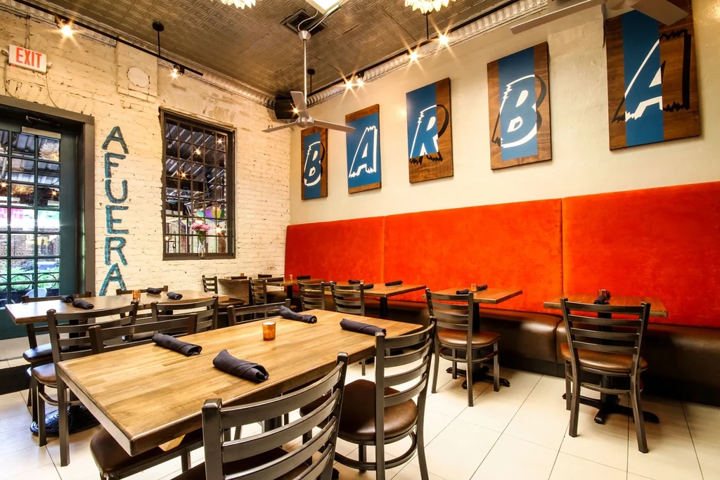 Restaurant interior: exposed brick, orange banquette, 'AFUERA' and 'BARBA' signs.