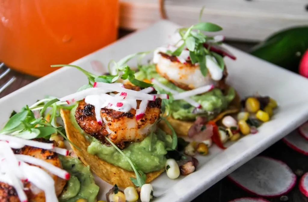 Three shrimp tostadas with guacamole, shrimp, and radish on a white plate.