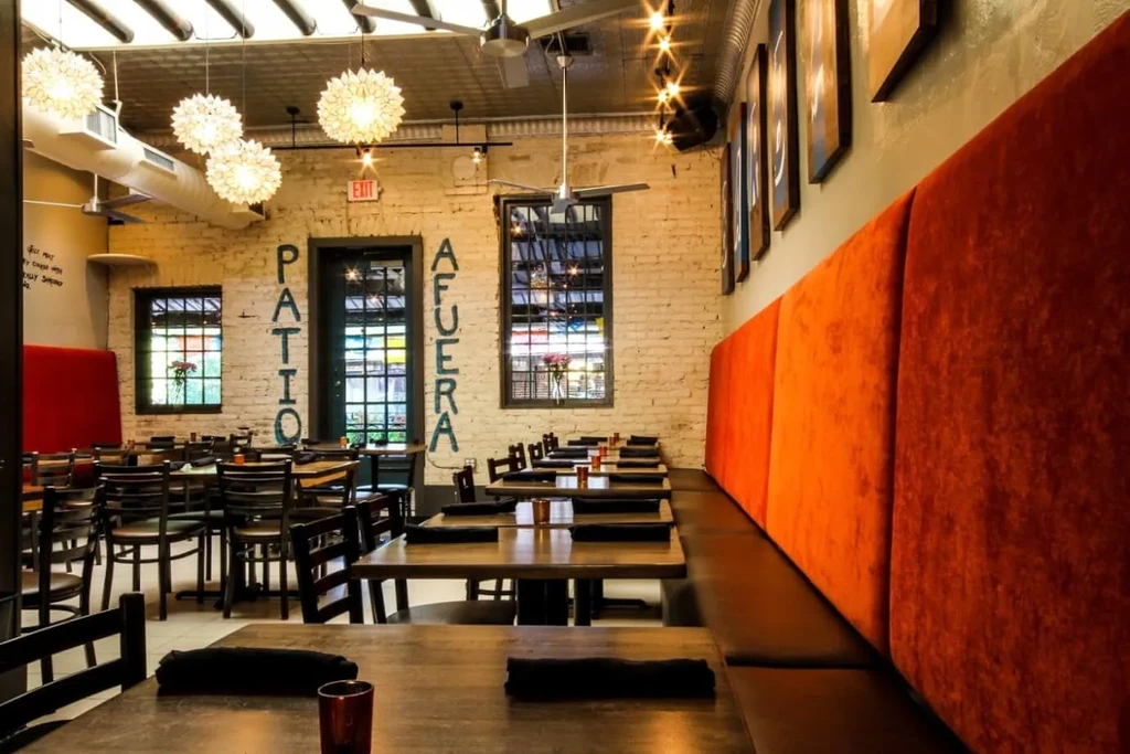 Empty restaurant with orange banquette, wooden tables, and starburst lights.