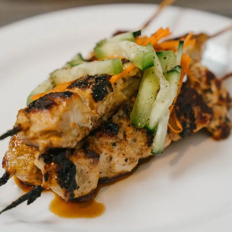 Grilled chicken or pork skewers with cucumber, carrot, and dark sauce.