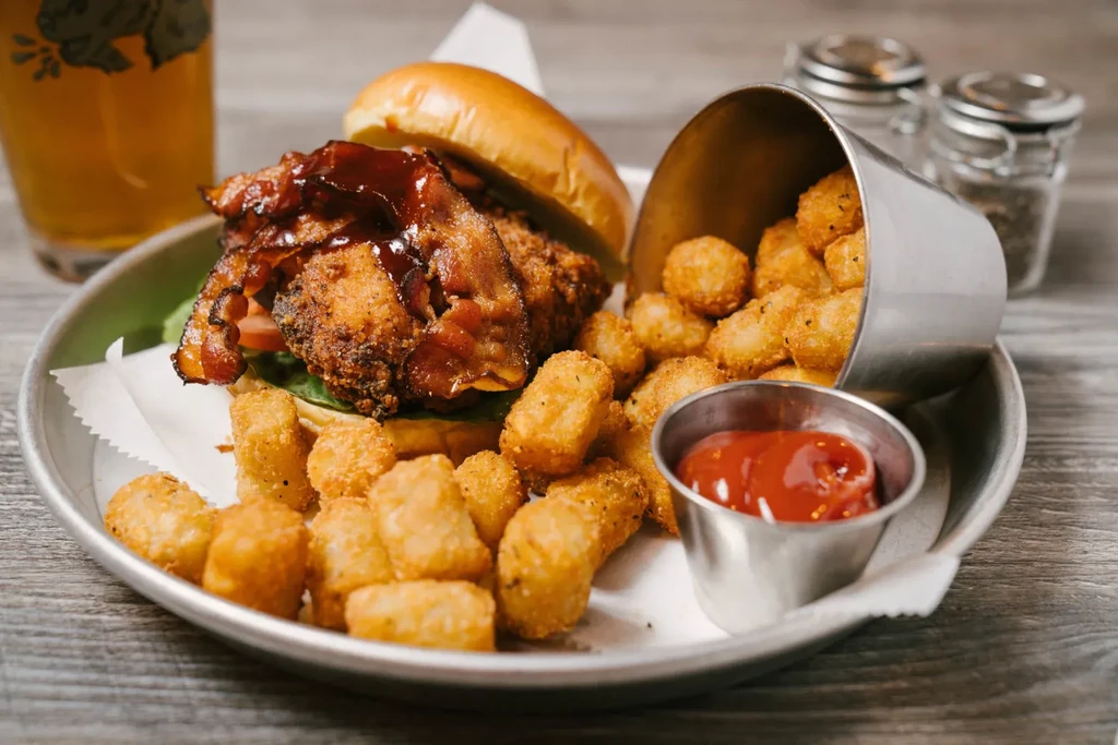 Crispy chicken burger with bacon, tater tots, ketchup, and beer.