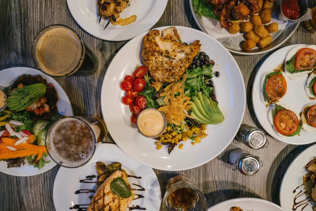 Overhead: rustic table covered with diverse plated dishes and drinks.