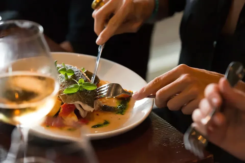 Close-up of hands cutting a beautifully plated fish dish at a restaurant.