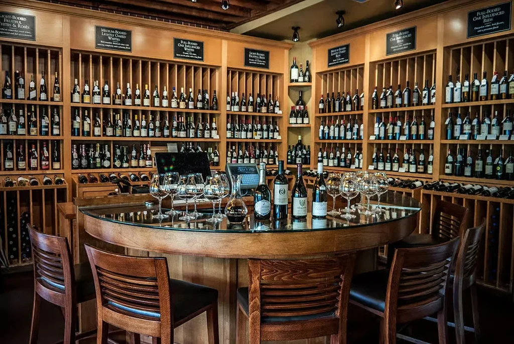 Organized wine room with tasting counter, bottles, glasses, and labeled shelves.