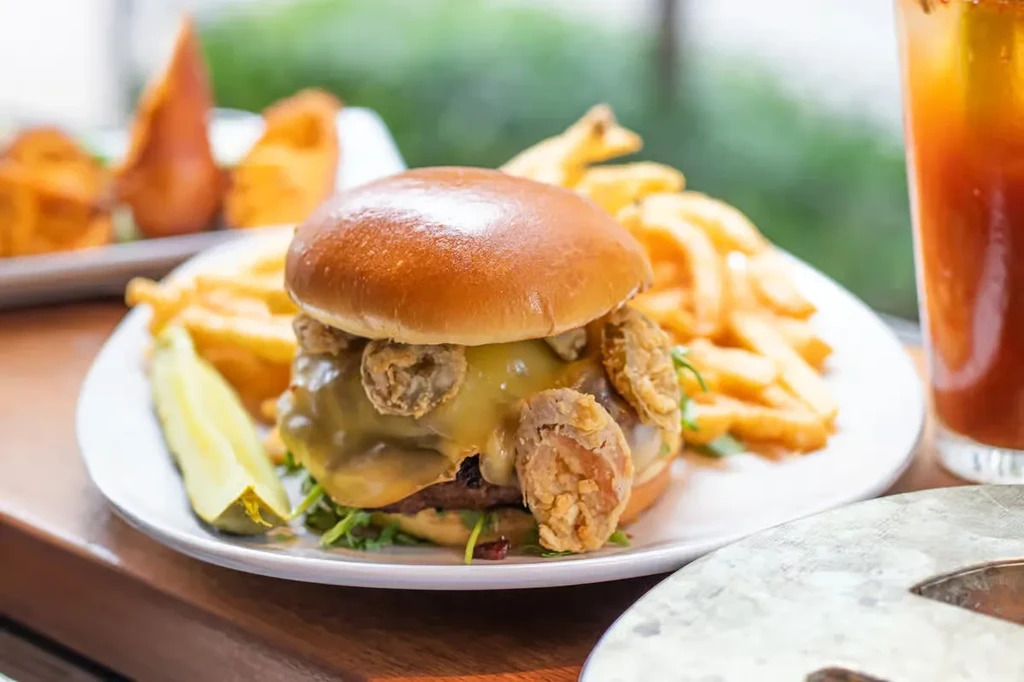 Close-up of a gourmet burger, golden fries, and a green pickle.