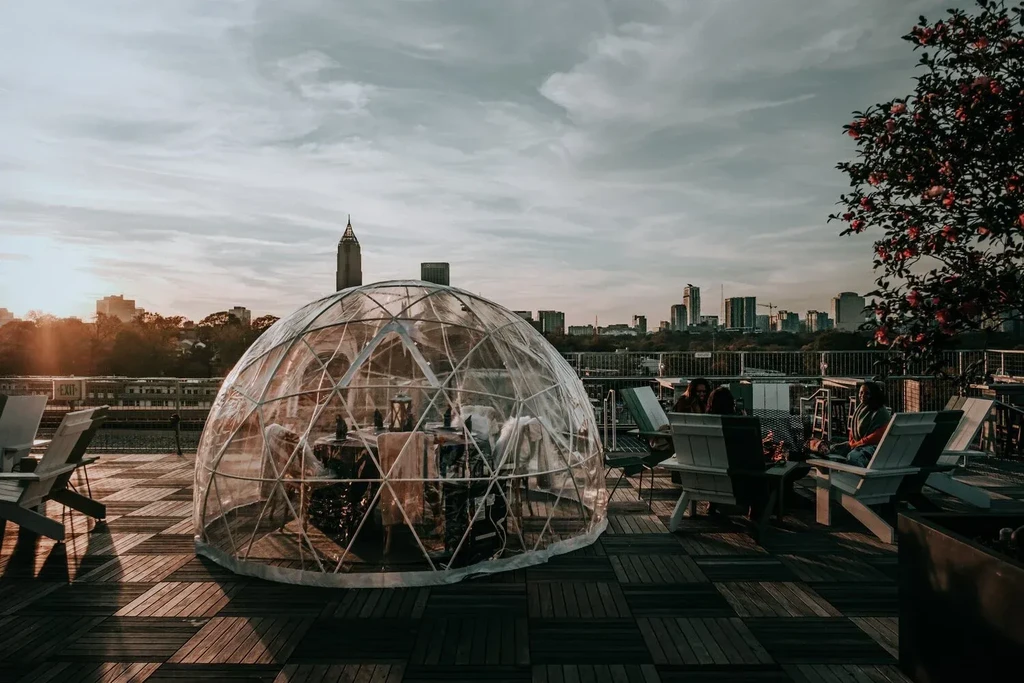 Rooftop geodesic private dining dome, city skyline at golden hour.