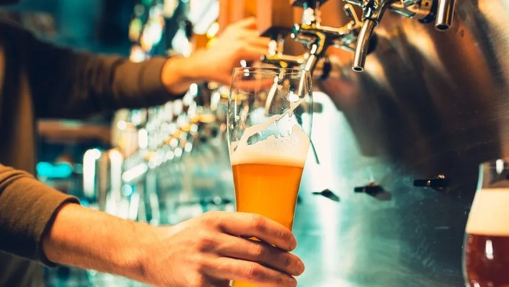 Close-up of hands holding golden beer, blurred taps behind.