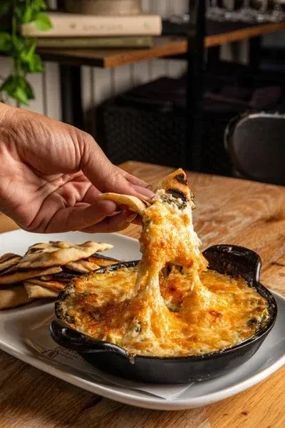 Hand dips grilled flatbread into stringy cheese dip in a skillet.