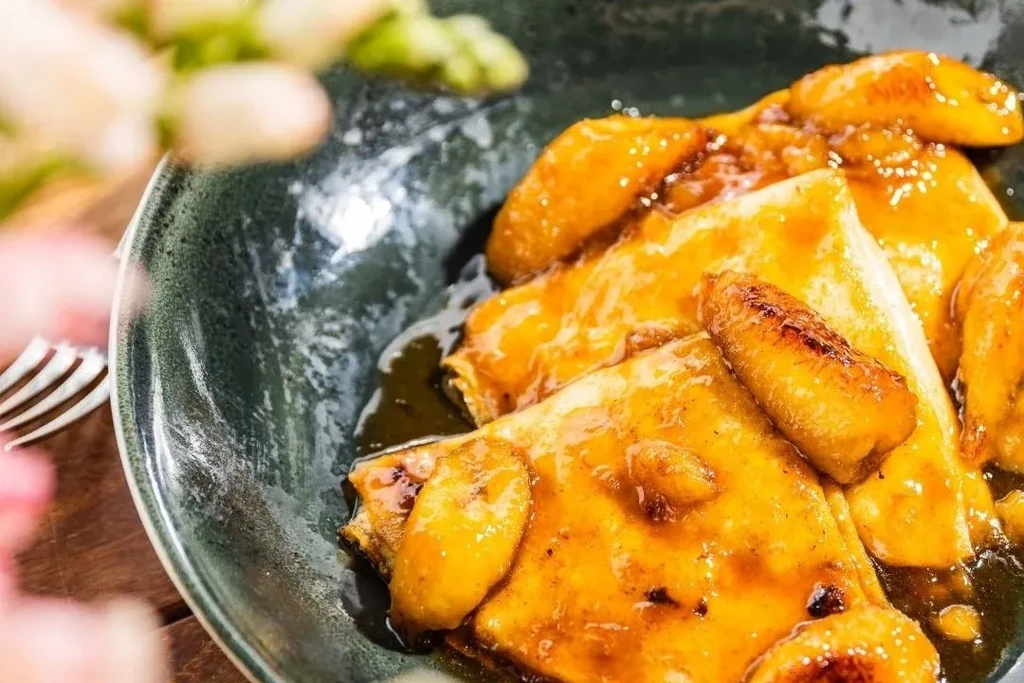 Crepes with golden caramel sauce and caramelized banana in a dark bowl.