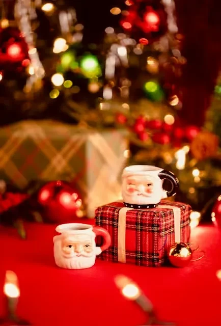 Two ceramic Santa mugs and a plaid gift box in a festive scene.