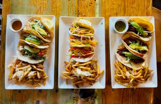 Overhead view of three plates of tacos and seasoned french fries.