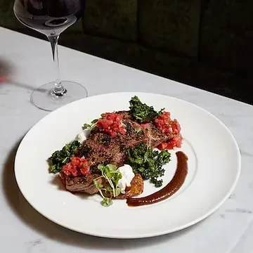 A plated steak dish with red salsa, green vegetables, and wine.