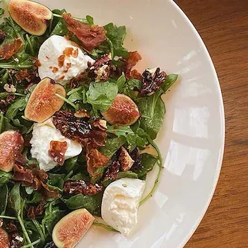 A close-up of a fresh salad with figs, creamy cheese, and prosciutto.