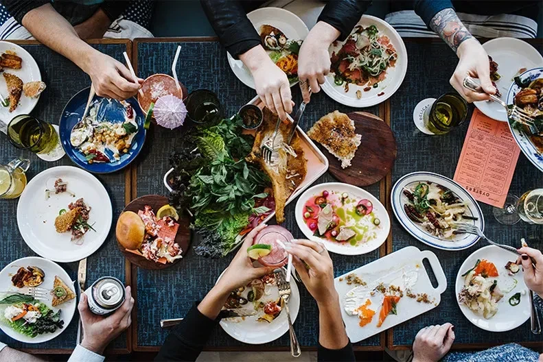 Overhead view of shared food, drinks, and hands at a restaurant.