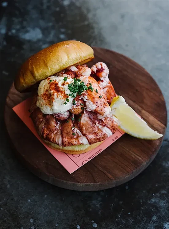 Lobster roll with creamy sauce, chives, lemon, on wooden board.