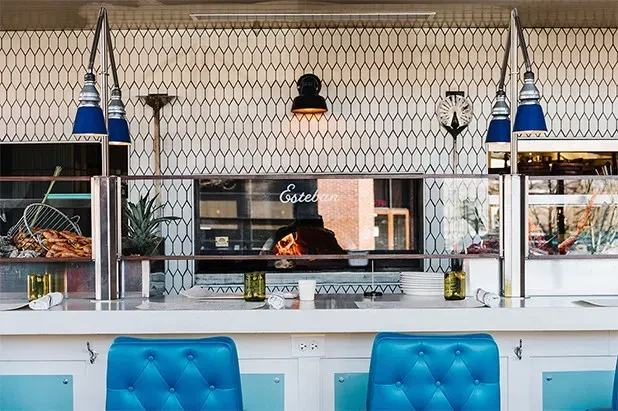 Esteban's modern restaurant interior with turquoise stools and a fiery pizza oven.