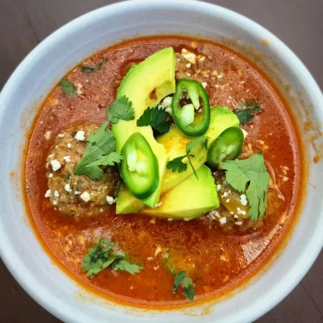 Hearty stew with meatballs, sliced avocado, cheese, cilantro, and jalapeños.
