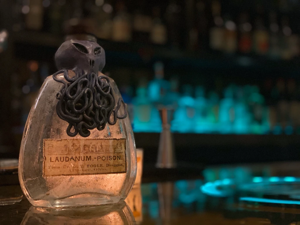 Ornate antique "LAUDANUM - POISON" bottle with tentacle stopper on bar.