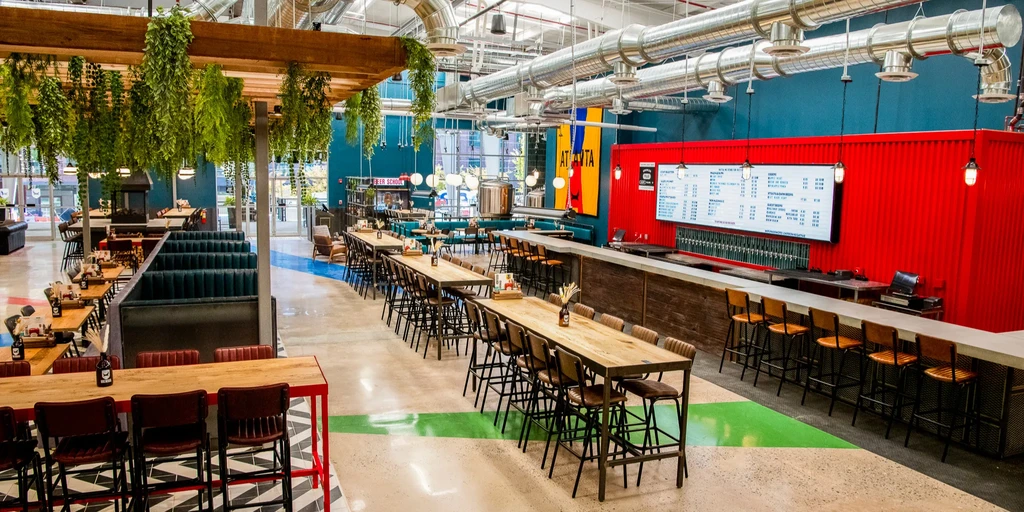 Modern restaurant interior with vibrant red/teal walls, green plants, and an Atlanta sign.