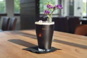 Dark drink with frothy head, ice, purple flowers in a cafe.