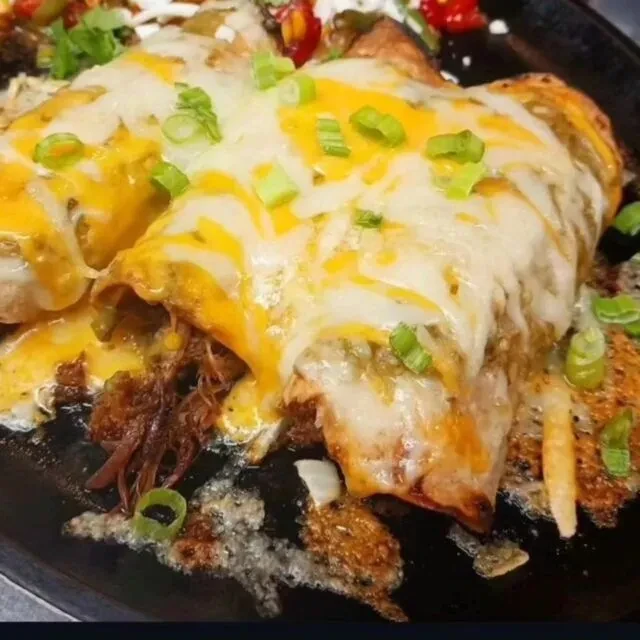 Two cheesy meat enchiladas with green sauce, garnished with green onions.