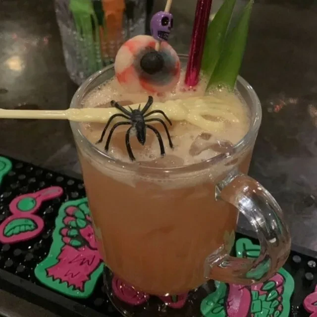 Halloween-themed orange cocktail in a mug, with spooky skull and eyeball.