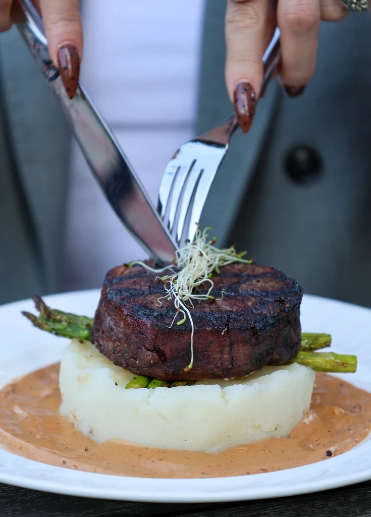 Hands cutting into a grilled steak with mashed potatoes and asparagus.