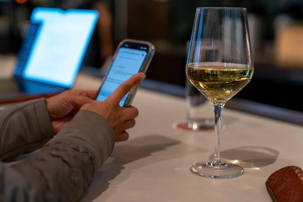 Hands interacting with a phone and a wine glass at a bar.