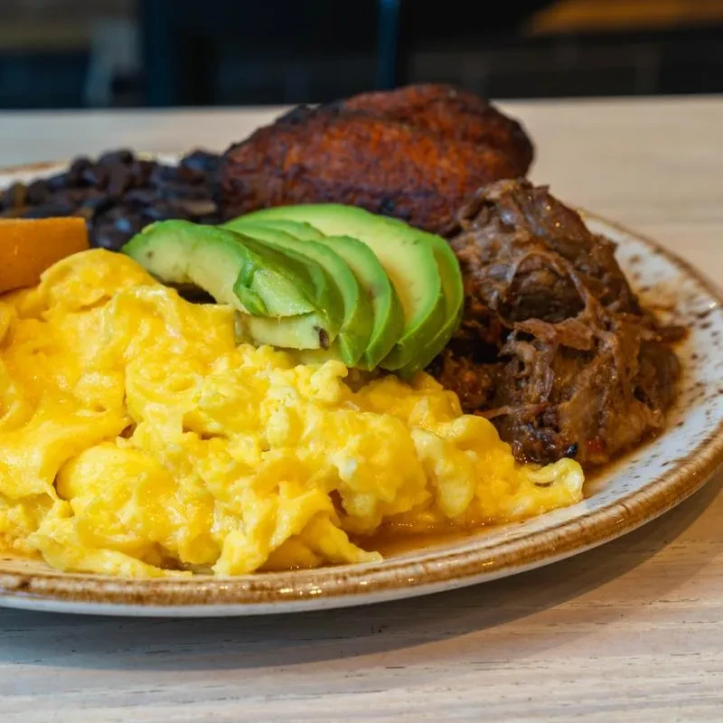 Generously portioned plate: scrambled eggs, avocado, shredded meat, plantains, black beans.