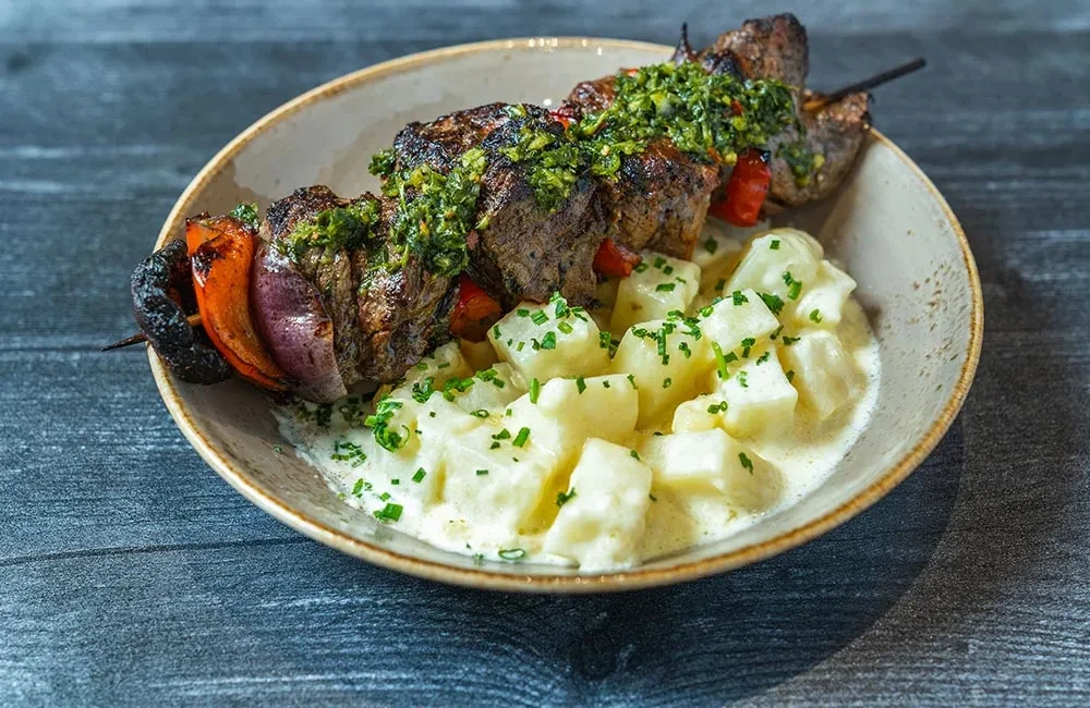 Grilled meat skewer, vibrant herb sauce, and creamy chive potatoes.