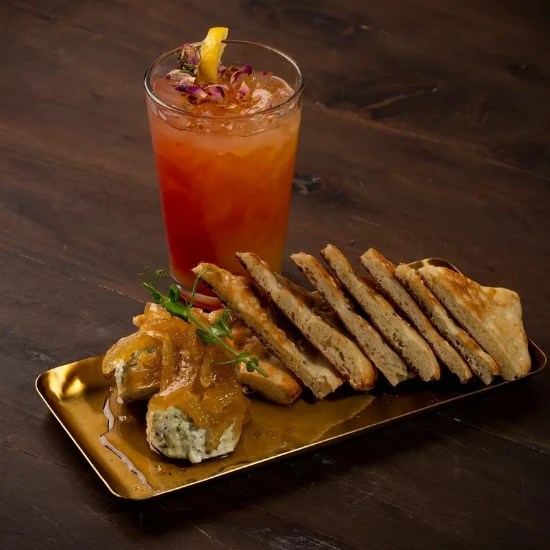 Amber drink, quenelles with chutney, and sliced flatbread on wood.