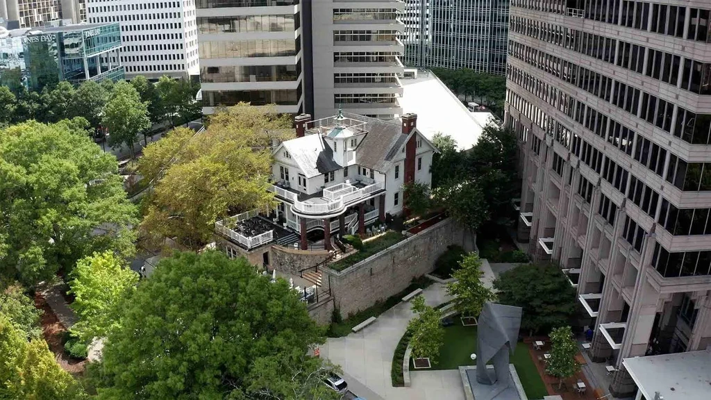 Historic white mansion amidst skyscrapers and a green city park.