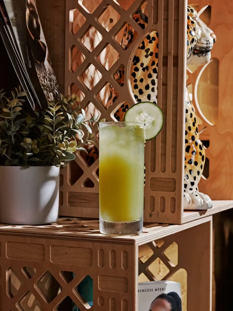 Icy green drink with cucumber, a spotted statue, and geometric wood decor.