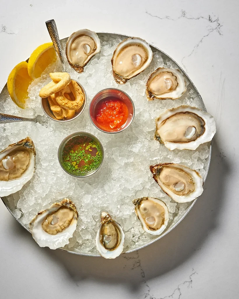 Eleven freshly shucked oysters on ice with lemon and condiments.