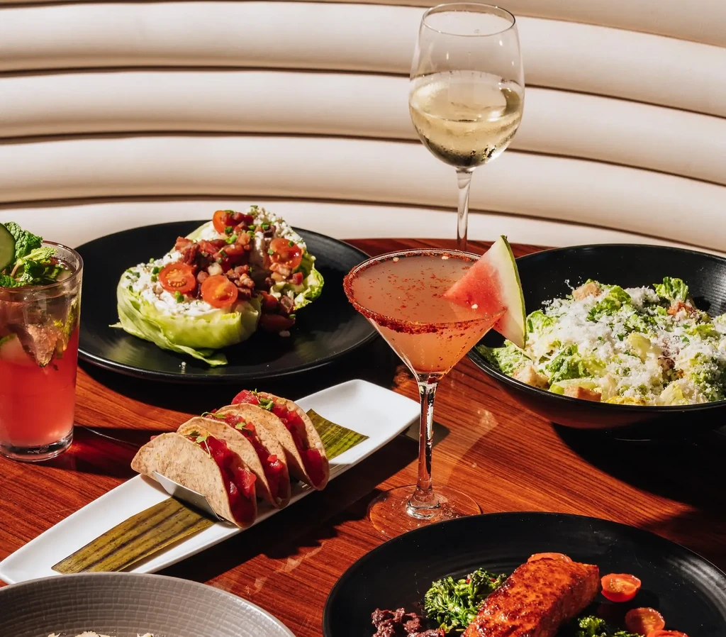 Multiple dishes and drinks: tacos, salads, grilled fish, and cocktails.