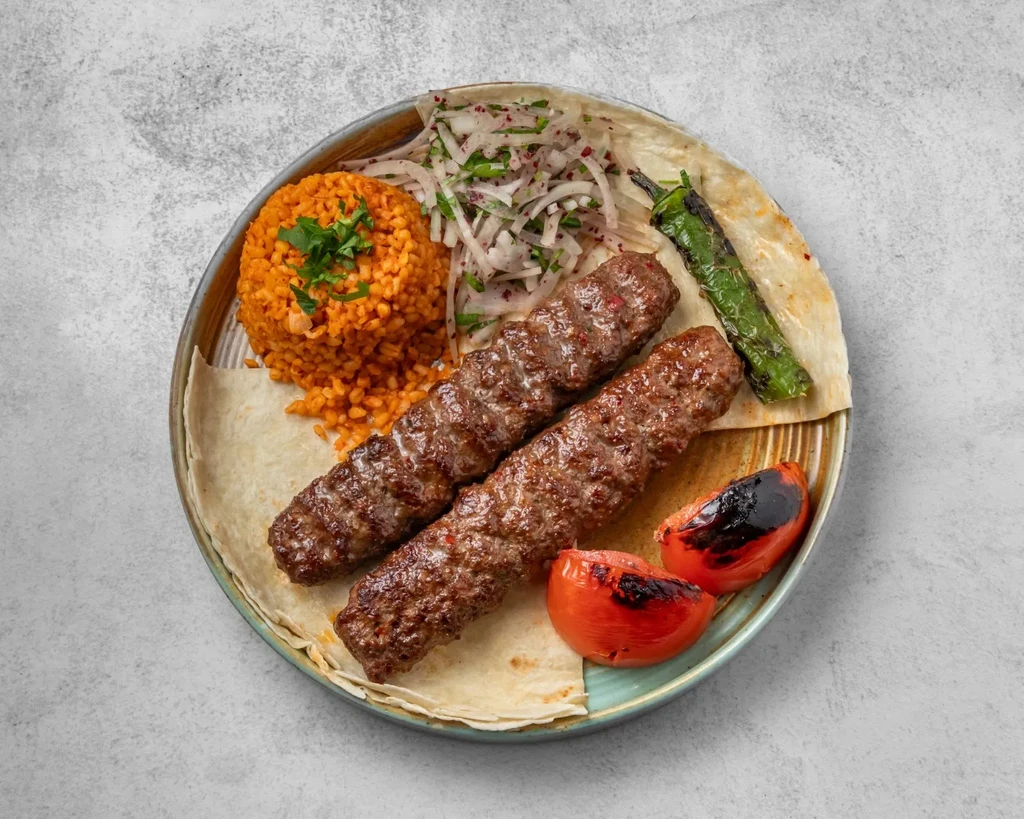 Grilled ground meat kebabs, pilaf, salad, and grilled vegetables on flatbread.