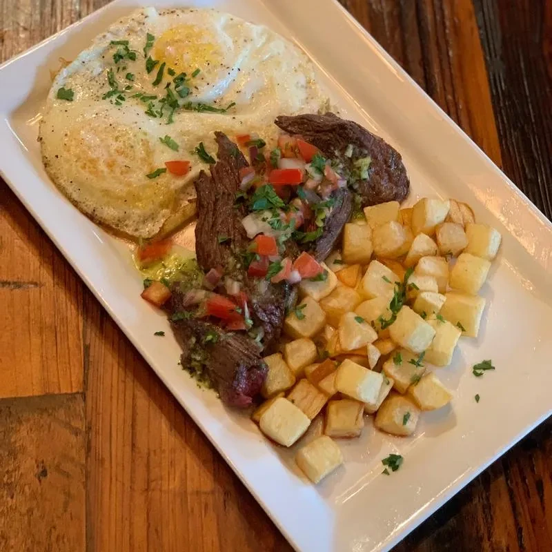 Plated breakfast with fried eggs, steak, diced potatoes, pico de gallo.