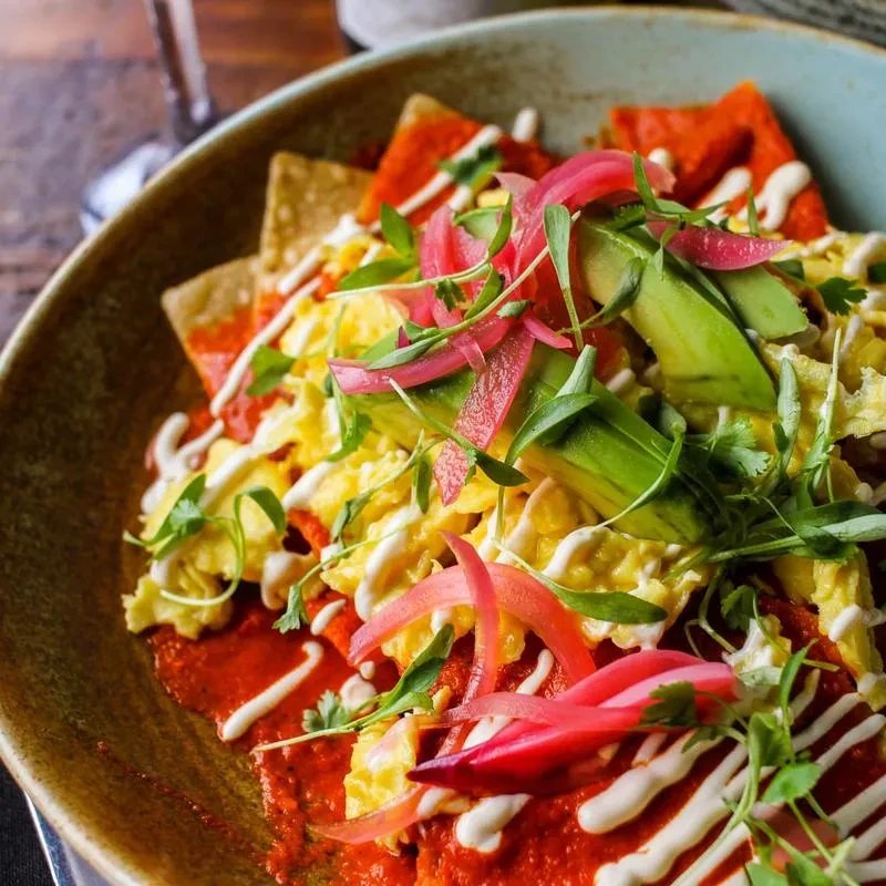 Chilaquiles, eggs, avocado, pickled onions, and crema in a blue bowl.