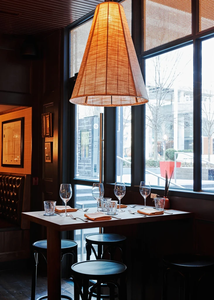 Restaurant high-top table under a large woven lampshade, with urban view.